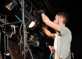 Photo of a crew member wearing a tool belt and gloves adjusting a light on a rig.