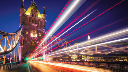 Tower Bridge lit up at night with blurred streaks of light running across the image showing the motion of passing car lights over a long exposure.