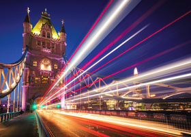 Tower Bridge lit up at night with blurred streaks of light running across the image showing the motion of passing car lights over a long exposure.