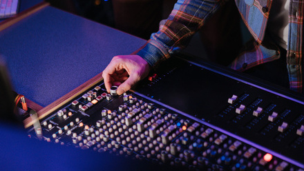 Close-up of a hand adjusting audio mixer sliders under neon lighting.