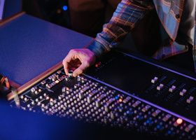 Close-up of a hand adjusting audio mixer sliders under neon lighting.