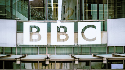 Photo of the outside of the BBC building in London, a close up on the logo in white on a modern, glass facade.