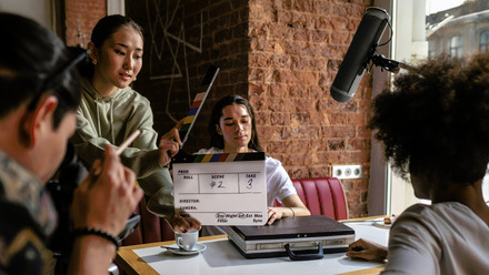 Diverse production crew shooting in a diner-style location. On person is holding a clapperboard in front of an actor.