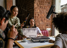 Diverse production crew shooting in a diner-style location. On person is holding a clapperboard in front of an actor.