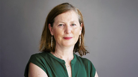 Headshot: Kitty Walshe, a woman with short brown hair styled with a side part, wearing a forest-green top and dangly earrings.