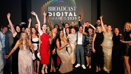 A large group of people dressed formally in glamorous outfits celebrate on a stage with a Broadcast Digital Awards logo behind them.