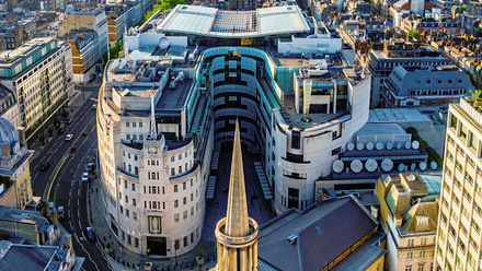 An aerial view of BBC Broadcasting House in Central London, a large curved building in brick and glass.