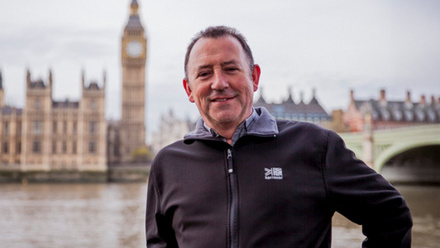 Headshot: Matthew Frank, a man with short hair, wearing a black fleece, stood in front of Big Ben.