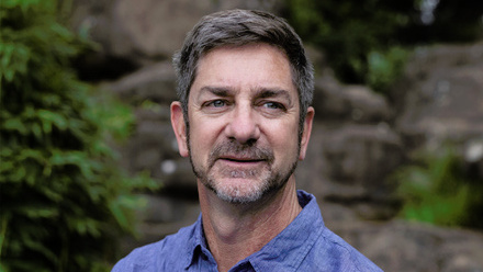 Headshot: Marc Lorber, a man with dark grey hair and a beard wearing a blue shirt.