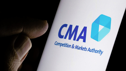 Photo image in low light of a bright white phone screen with the CMA Logo on it and a thumb and forefinger poised next to it.