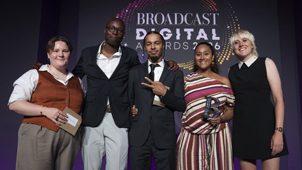 Five people pose for the camera, one holding an award, in front of a large digital screen with the Broadcast Digital Awards logo on it.
