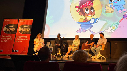 A stage with five speakers on it, with a large screen behind them showing an animated scene in bright colours.