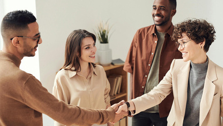 Four people making a deal with two people shaking hands.
