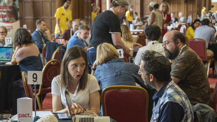 A large room full of people having meetings around small round tables.