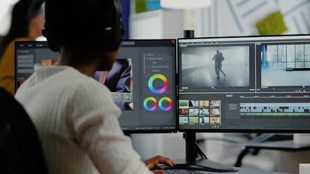 Over shoulder image of an editor at work, with two monitors with editing software open on them.