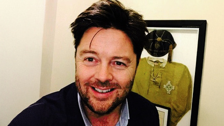 Headshot: Chris Jones, a man with dark brown hair and a beard wearing a blue shirt and blazer.