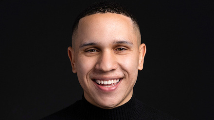 Headshot: Jordan Schwarzenberger, a man with short dark hair wearing a black polo neck top on a black background.