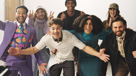 A diverse production crew celebrate the shoot wrap, posing for the camera with celebratory expressions and gestures.
