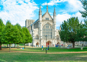 Summer time view of Winchester Cathedral west front in Hampshire surrounded by trees.