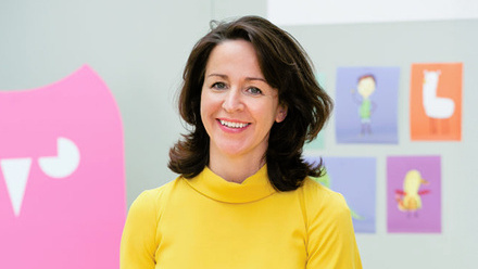 Headshot: Grainne McGuinness, a woman with short, dark-brown hair wearing a bright yellow long-sleeve top.