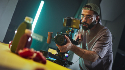 A videographer points a small camera towards a display of food and drink products on a table.