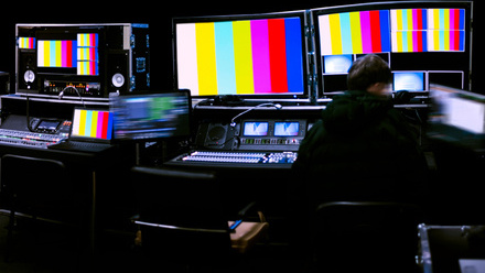 Image showing flat TV monitors with broadcast colour bars on them and an operator sitting at a desk in front of them.