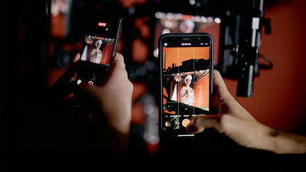 Close-up of two people holding phones and recording camera equipment on a drama production set.