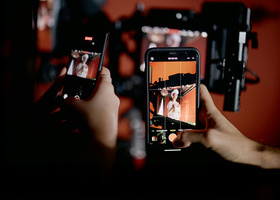 Close-up of two people holding phones and recording camera equipment on a drama production set.