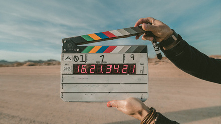 A person holding a Clapperboard in front of a sand dunes background.