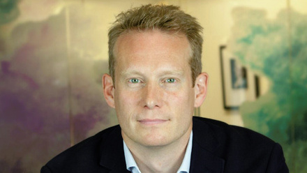 Headshot: Tom Manwaring, a man with short, blonde hair wearing a shirt and blazer.