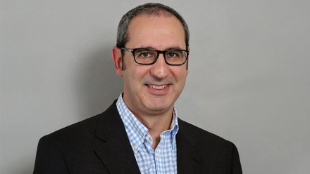 Headshot: Sammy Nourmand, a man with black glasses wearing a blue checked shirt and a navy blazer.