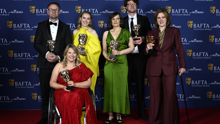 The team behind Code of Silence pose in front of blue and white BAFTA branding holding BAFTA statuettes.