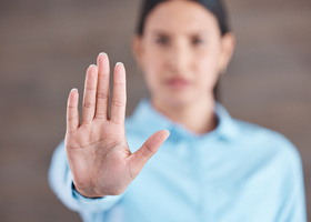 Photo of a woman holding her hand up to the camera. Her hand is in focus but her face and body behind it are out of focus.