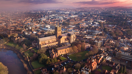 Aerial view of Worcester with the Cathedral prominent in the middle of the image and a purple sky above the horizon.