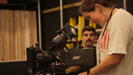 Person smiling and operating a camera in an industrial room, there is another person in the background observing.