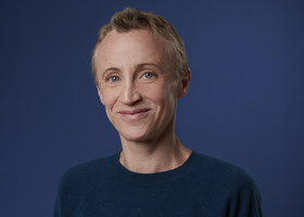 Headshot: Sam Margaritis, a woman with very short, fair hair wearing a navy blue top and smiling to camera.