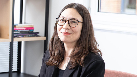 Headshot: Emily Oyama, a woman with long brown hair wearing glasses and a black jacket and top.
