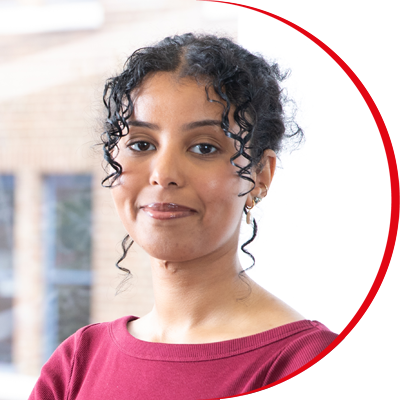 Headshot: Lisa Tesfai, a woman with curly dark hair tied back, wearing a red top.