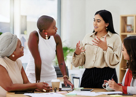 Diverse team of business women talking and brainstorming around a table in an office.