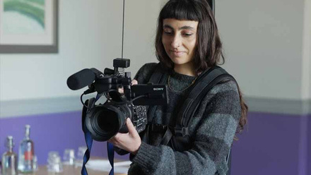 A camera bootcamp participant wearing a stripe jumper and operating a camera.