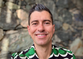 Headshot: Jason Mitchell, a man with dark brown hair and grey quiff wearing a green and black patterned shirt.