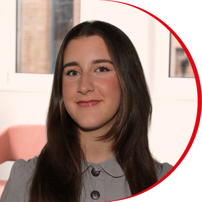 Headshot: Chloe Holt, a young woman with long brown hair wearing a grey top with black buttons.