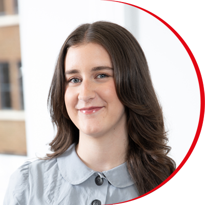 Headshot: Chloe Holt, a young woman with long brown hair wearing a grey top with black buttons.