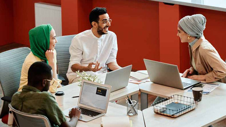 A group of diverse coworkers engaging in a collaborative discussion with laptops in a modern office setting.