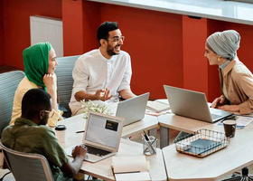 A group of diverse coworkers engaging in a collaborative discussion with laptops in a modern office setting.