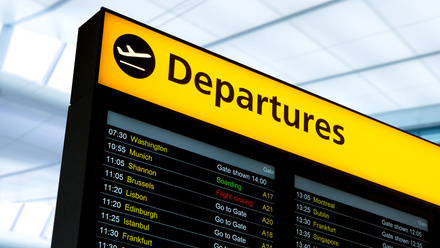 Close-up of airport departures board at a UK airport, with a yellow strip at the top and a black digital board with location names on it.