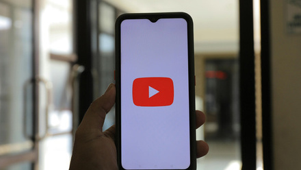 A hand holding a smartphone with the YouTube logo displayed.