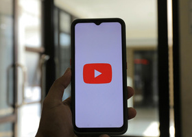 A hand holding a smartphone with the YouTube logo displayed.