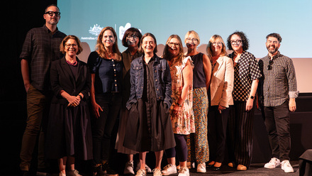 A group of people stand in a line in front of a large, lit digital screen.