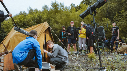 Camera crew Filming a tent in a rural location on rough terrain with trees in the background.
